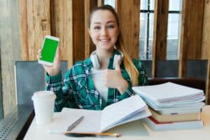 Etudiante à son bureau devant livre et cahier et avec smartphone.