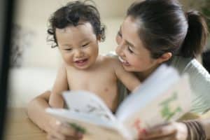 Une mère raconte une histoire devant un livre ouvert à son bébé de 1 an qui rit avec elle en regardant le livre.